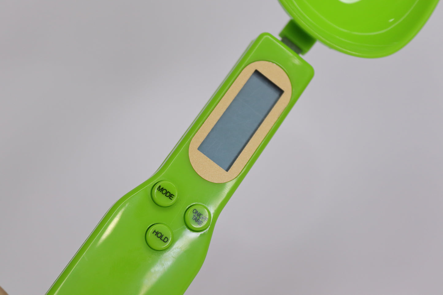 A close-up of a digital spoon scale featuring an LCD display and multiple buttons for mode selection, hold function, and tare, designed for precise kitchen measurements of ingredients like tea, coffee, and spices.