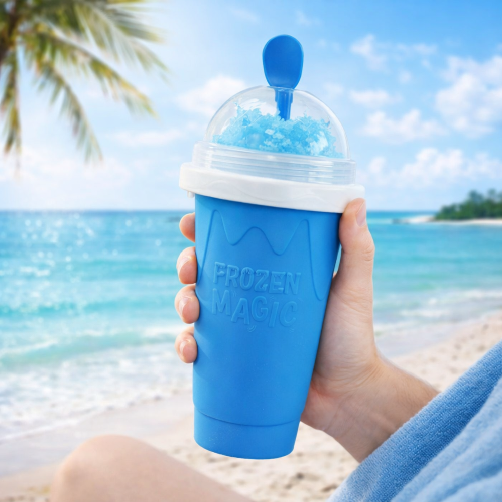 Hand holding blue Frozen Magic slushy maker cup on the beach with ocean and palm trees in the background.